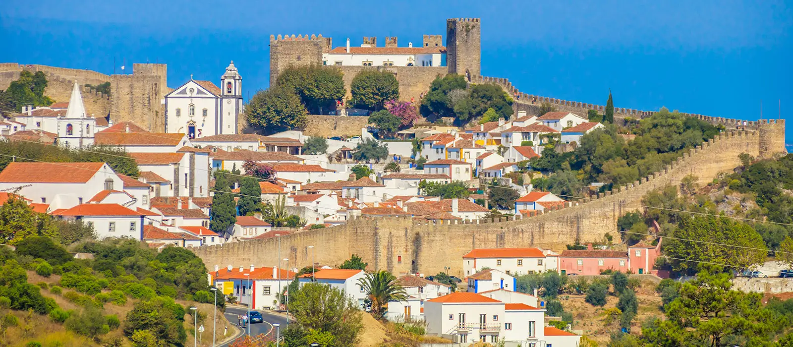 A view of the beautifully preserved medieval town of Óbidos, featuring historic stone architecture and narrow, winding cobbled streets.