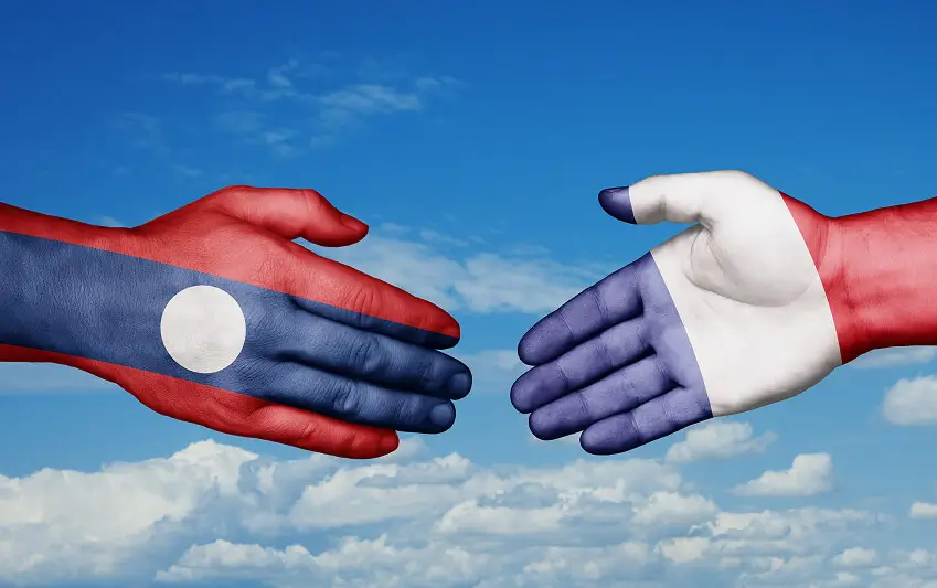 Hands painted with Laos and France flags shaking against a sky background symbolising international business cooperation and European expansion into Southeast Asia.
